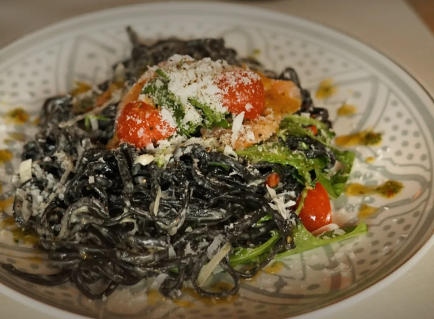 Schwarze Bandnudeln mit Lachs, Kirschtomaten und Rucola auf einem gemusterten Teller